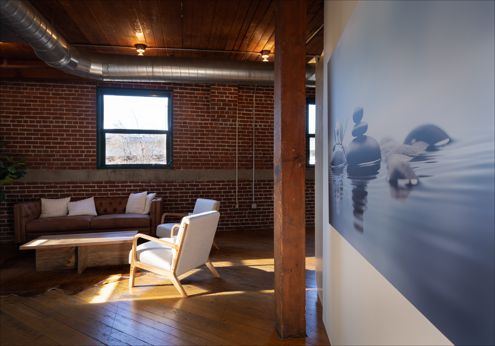 Individual Experience 5 Cozy retreat space featuring a brown leather sofa and light wooden coffee table, with serene stone stack artwork on the wall, emphasizing a calming atmosphere for the women's only retreat at Experience Onward.