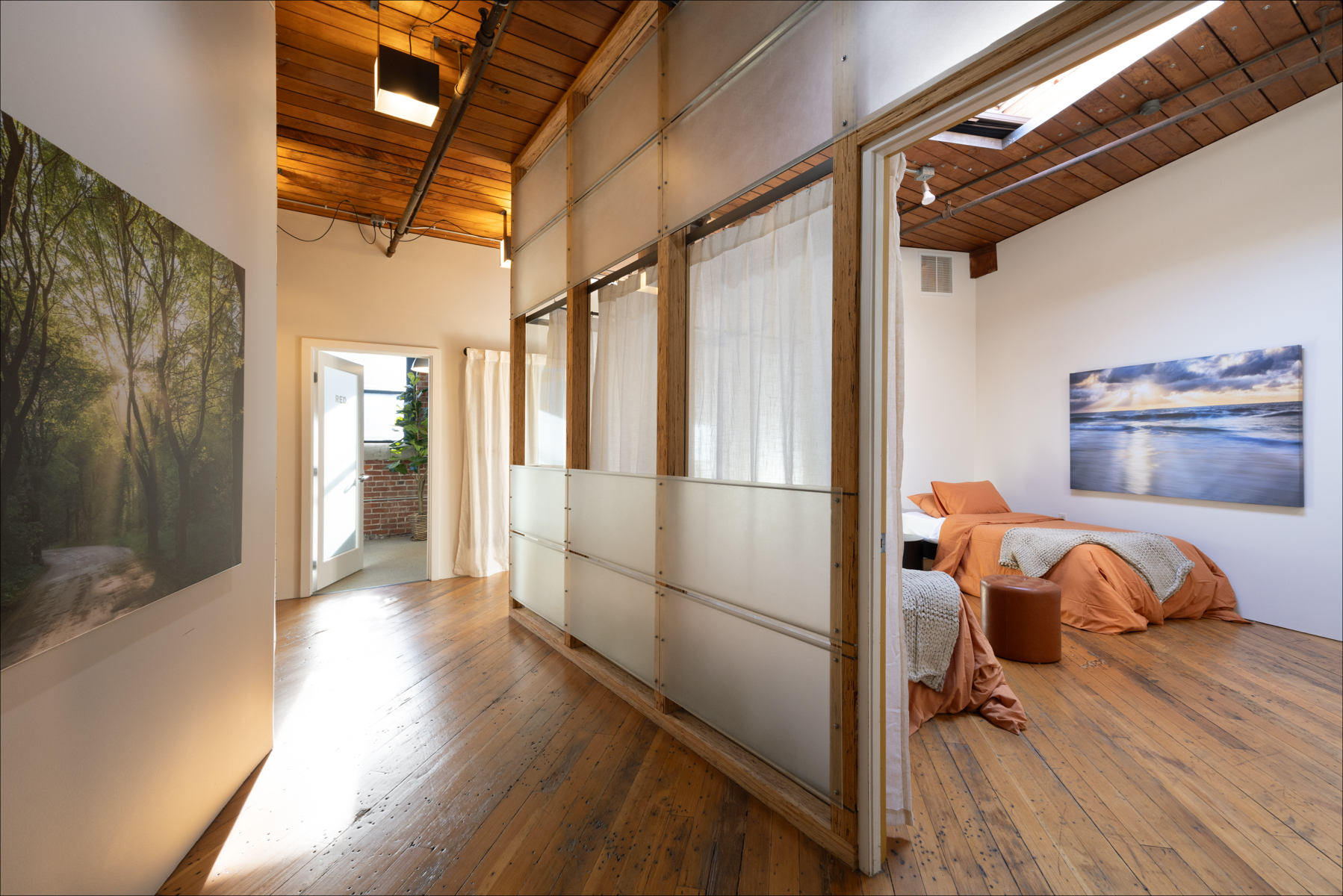 Individual Experience 1 Cozy retreat room with wooden floors, soft orange bedding, and a serene ocean landscape painting, designed for a women's only healing experience at Experience Onward.